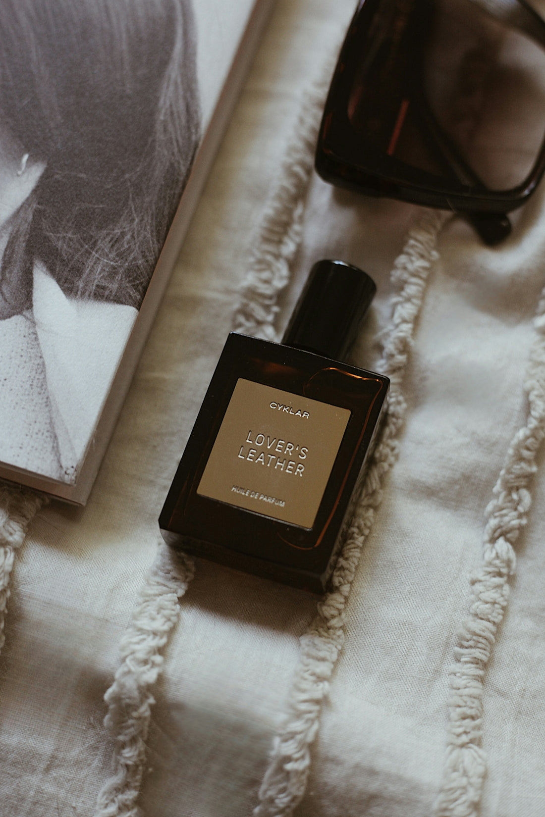Perfume bottle on a bed next to magazine.