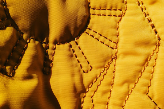 Close up of yellow fabric with stitched details.